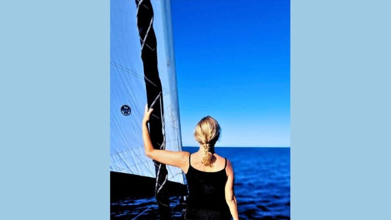 Margaret Marchuk stands on her sailboat, facing the open sea under a bright blue sky, symbolizing courage, transformation, and her journey beyond fear.